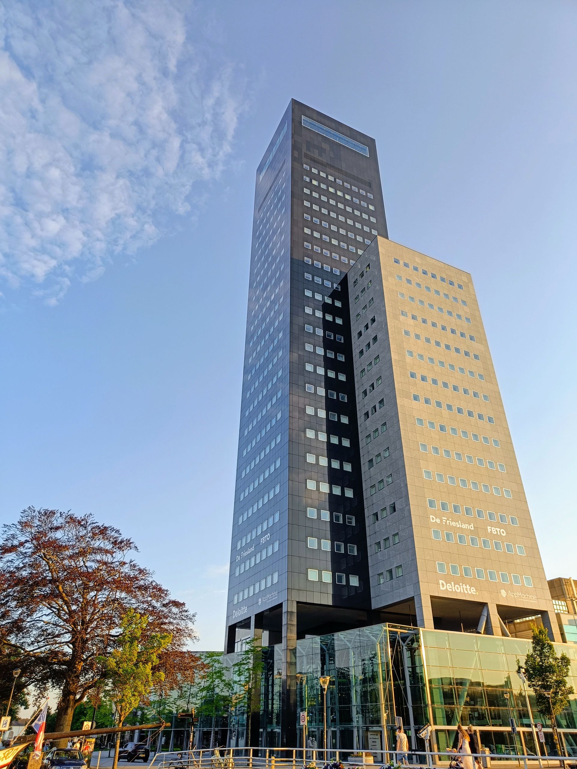 Hoog, modern gebouw met een donkere gevel, een lichtgekleurde zijkant en een blauwe lucht.