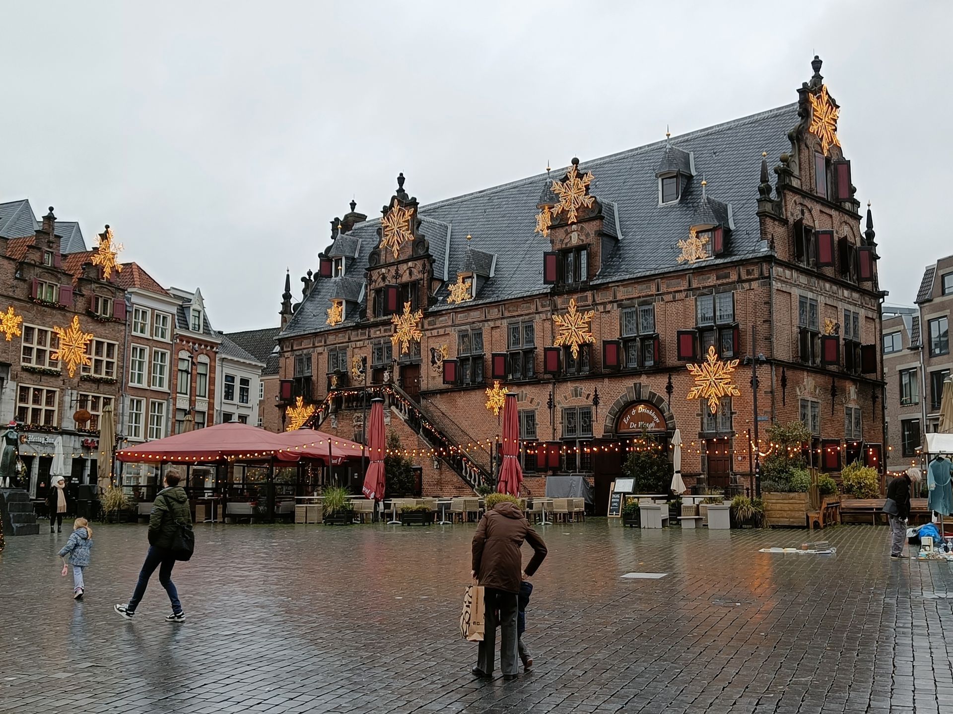 Historisch gebouw met kerstverlichting op een plein met wat mensen, op een regenachtige dag.