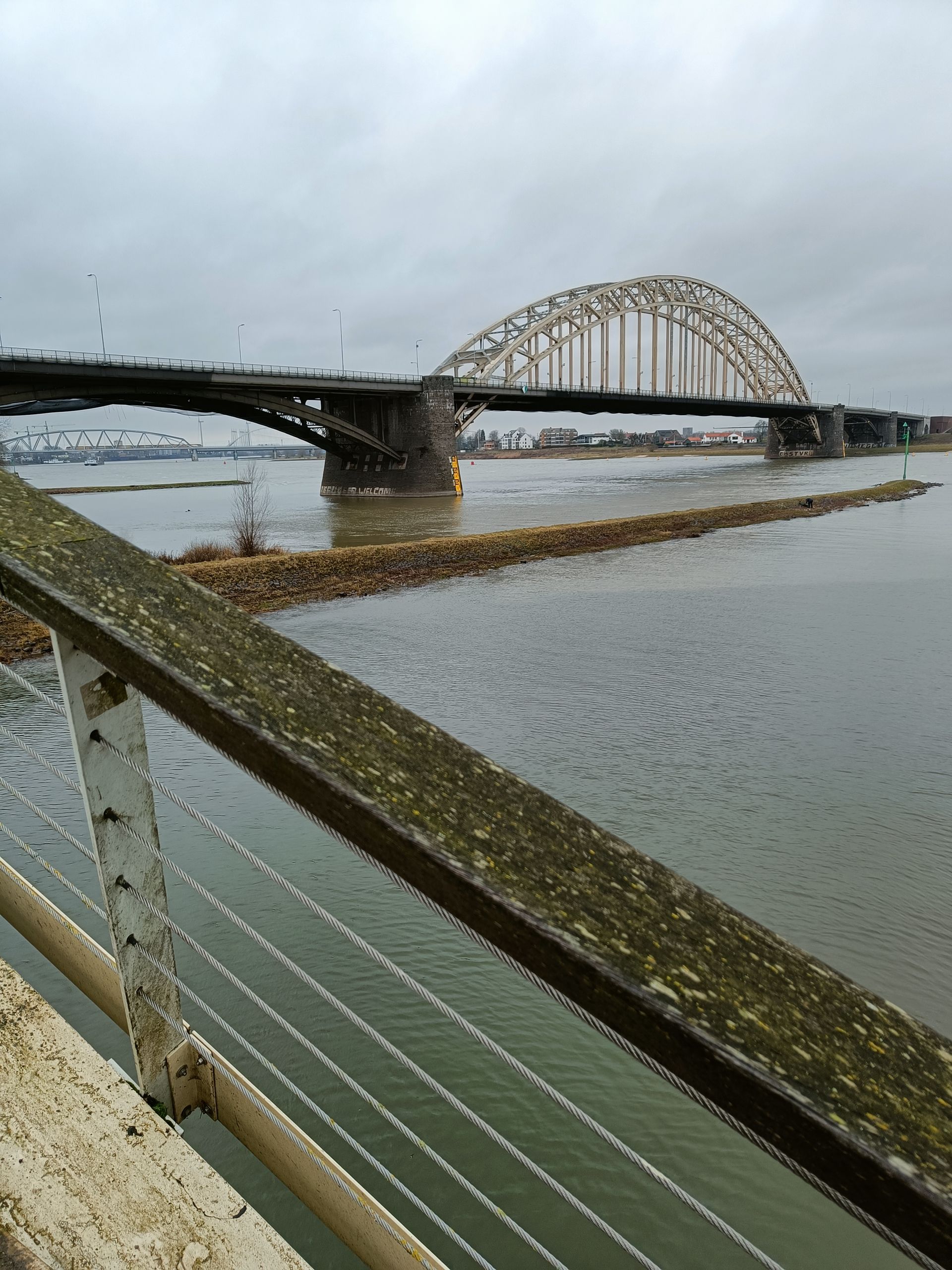 Brug over het water met een grote boog, bewolkte lucht. Uitzicht vanaf een lager niveau met een reling.