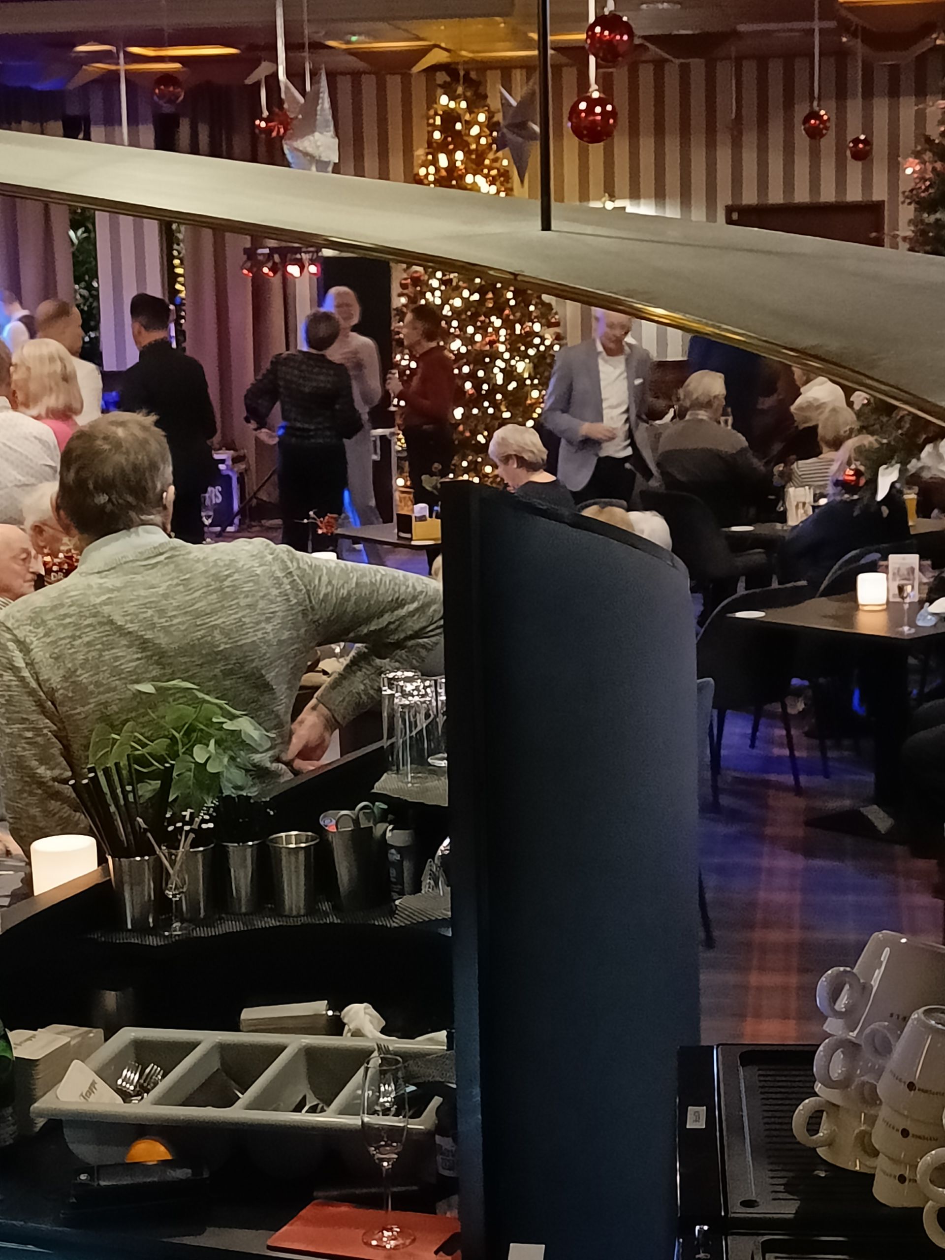 Interieur van een bar en restaurant, versierd voor de feestdagen, met gasten en barpersoneel.
