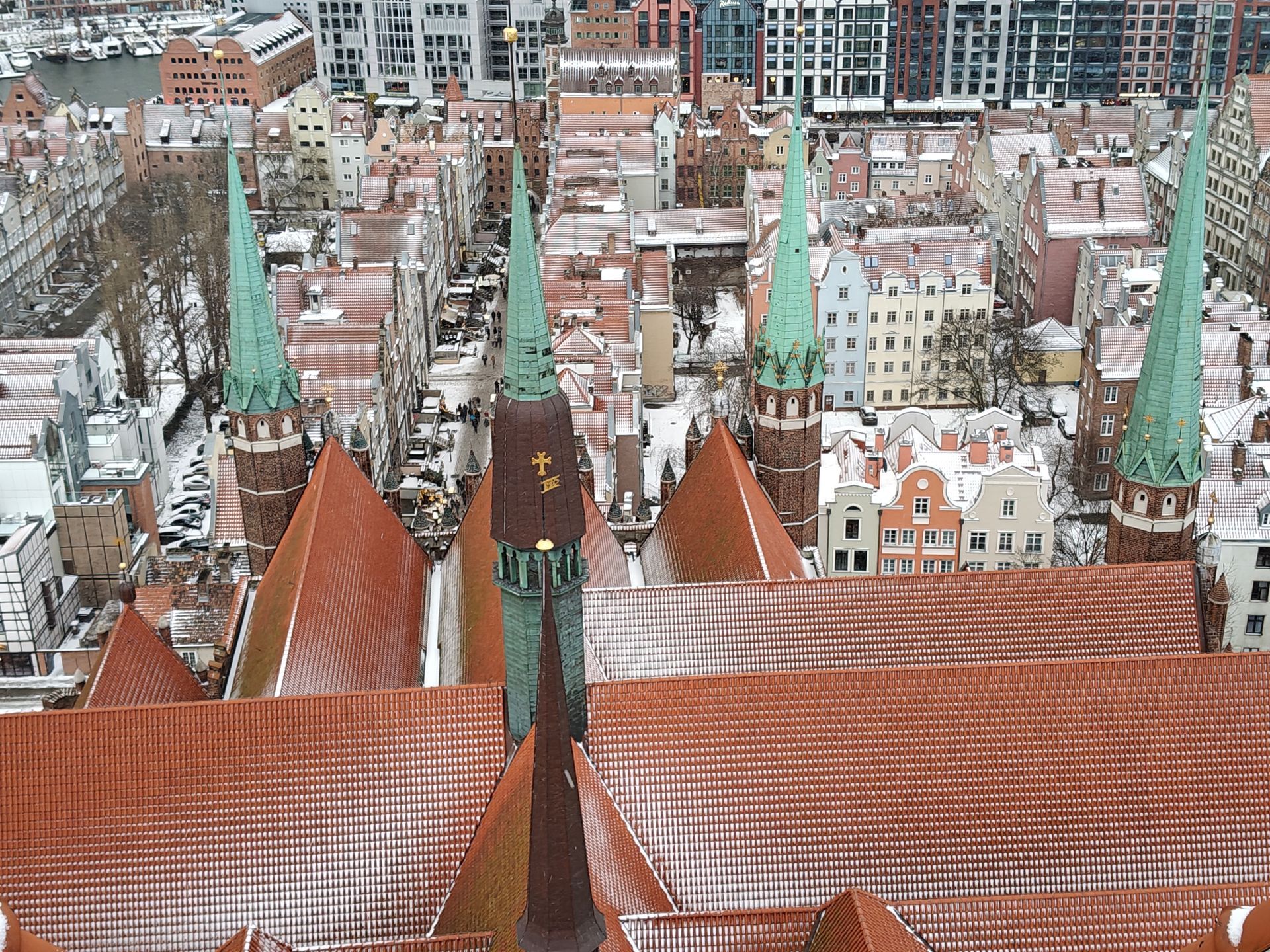 Een hoog perspectief van een stad met rode pannendaken, groene torens en sneeuw. De gebouwen staan dicht op elkaar.