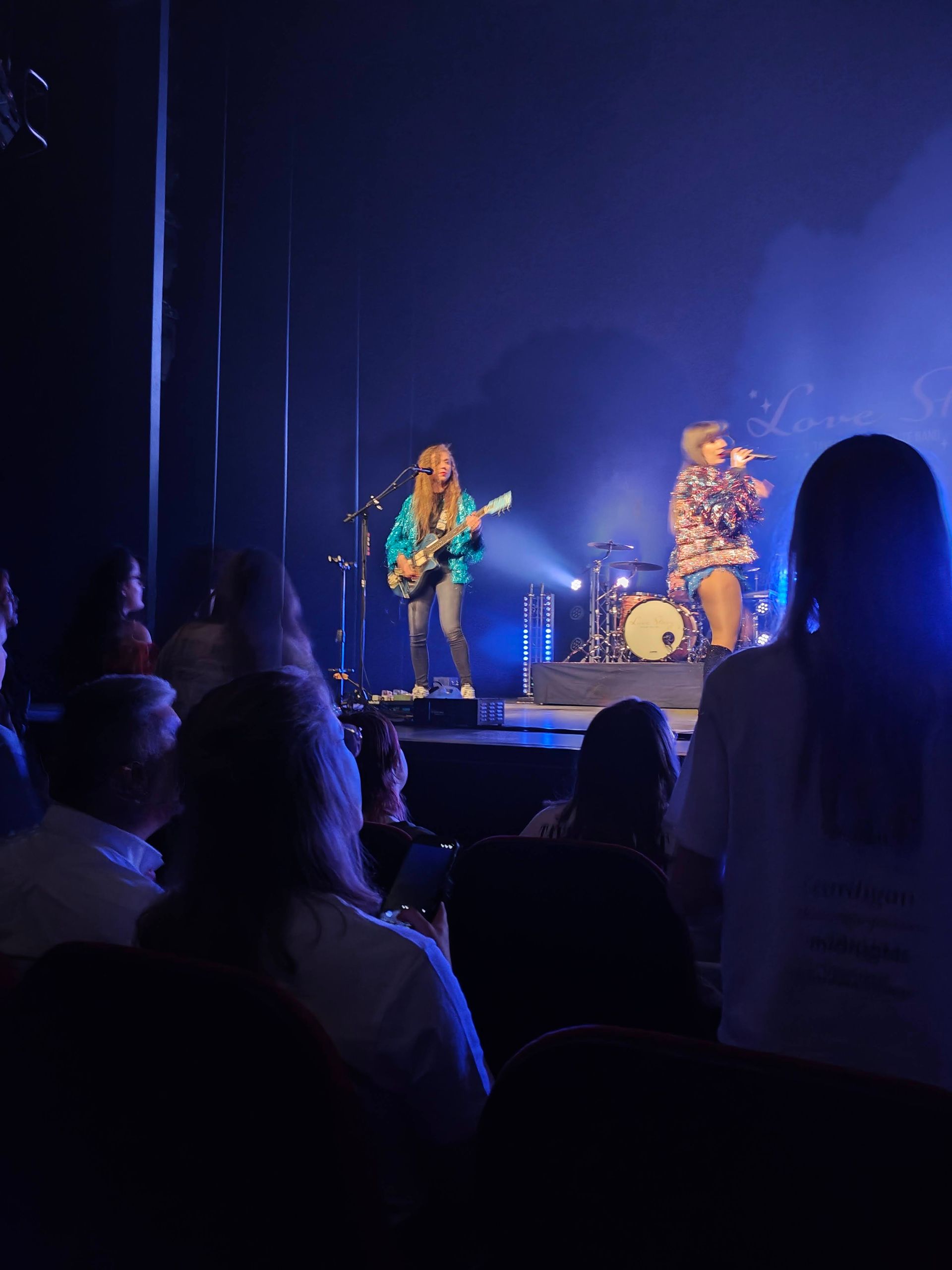 Twee muzikanten treden op een blauw verlicht podium op voor een zittend publiek.