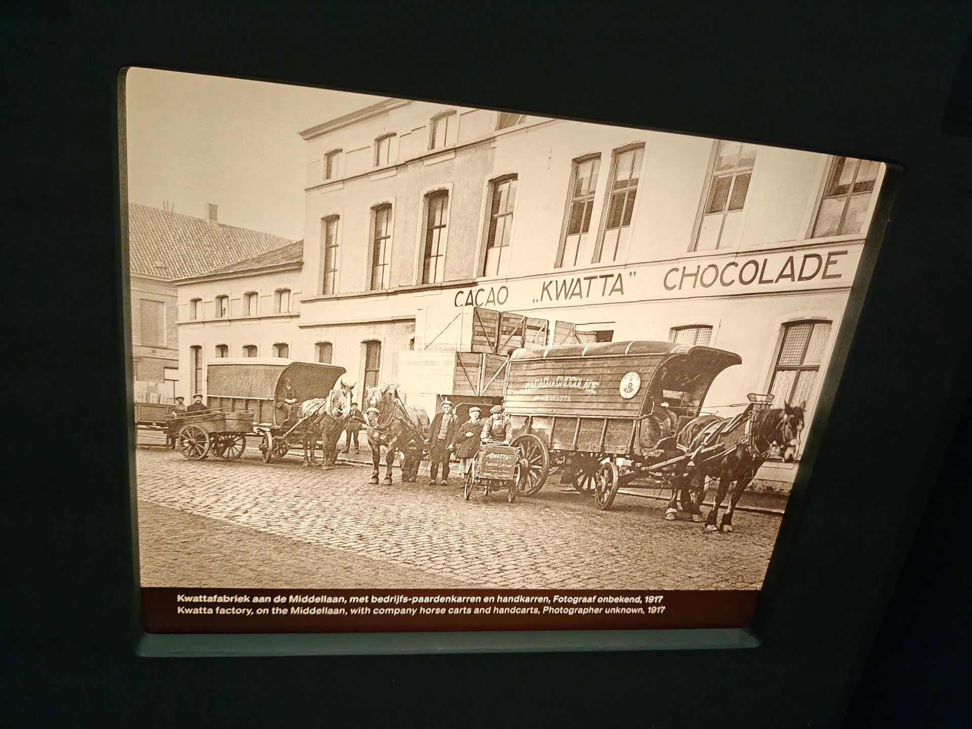 Historische sepiafoto van een paardenkar voor een gebouw met het opschrift 