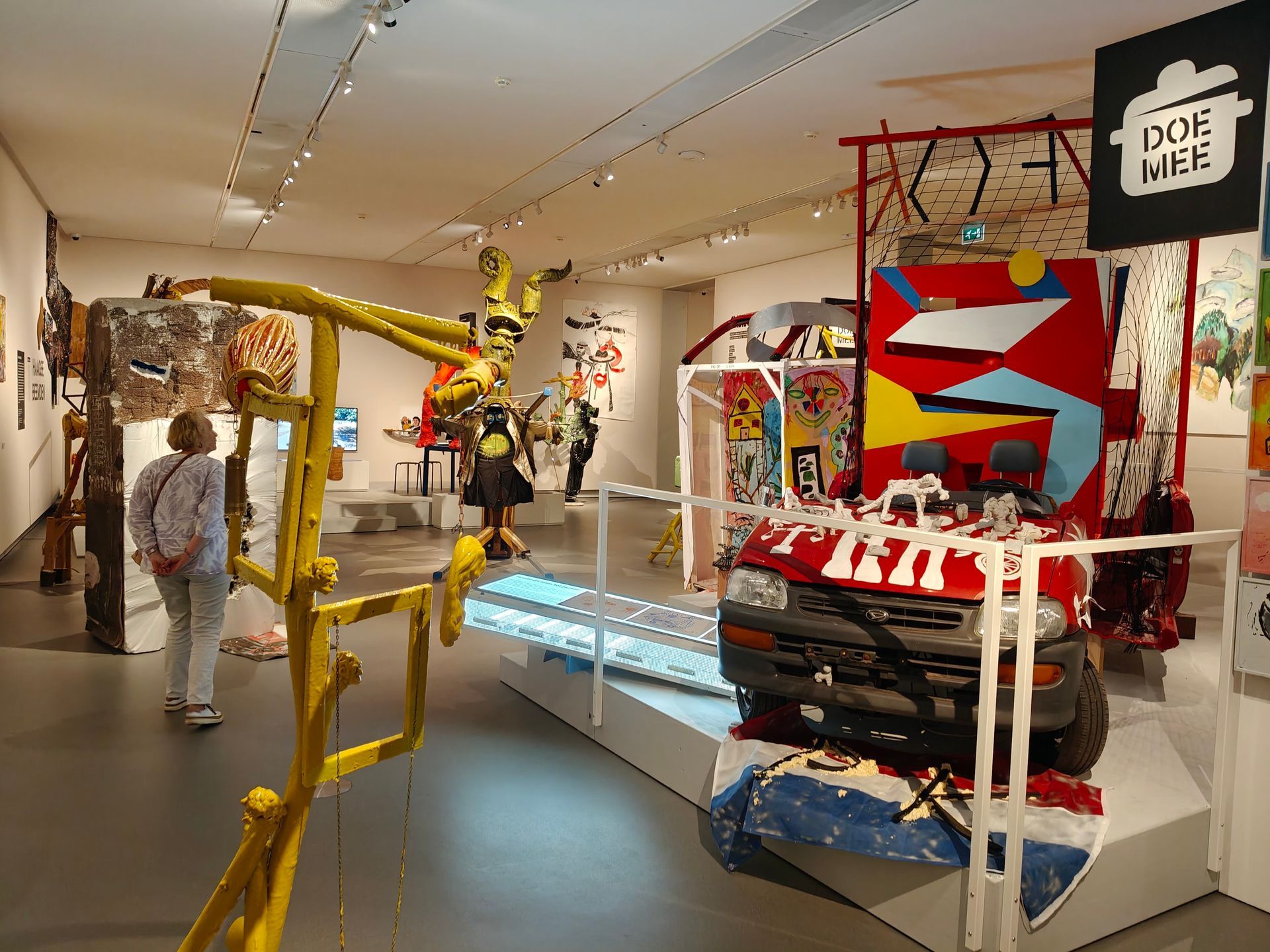 Kunstgalerie met kleurrijke installaties van gemengde technieken en een persoon die door de tentoonstelling loopt.