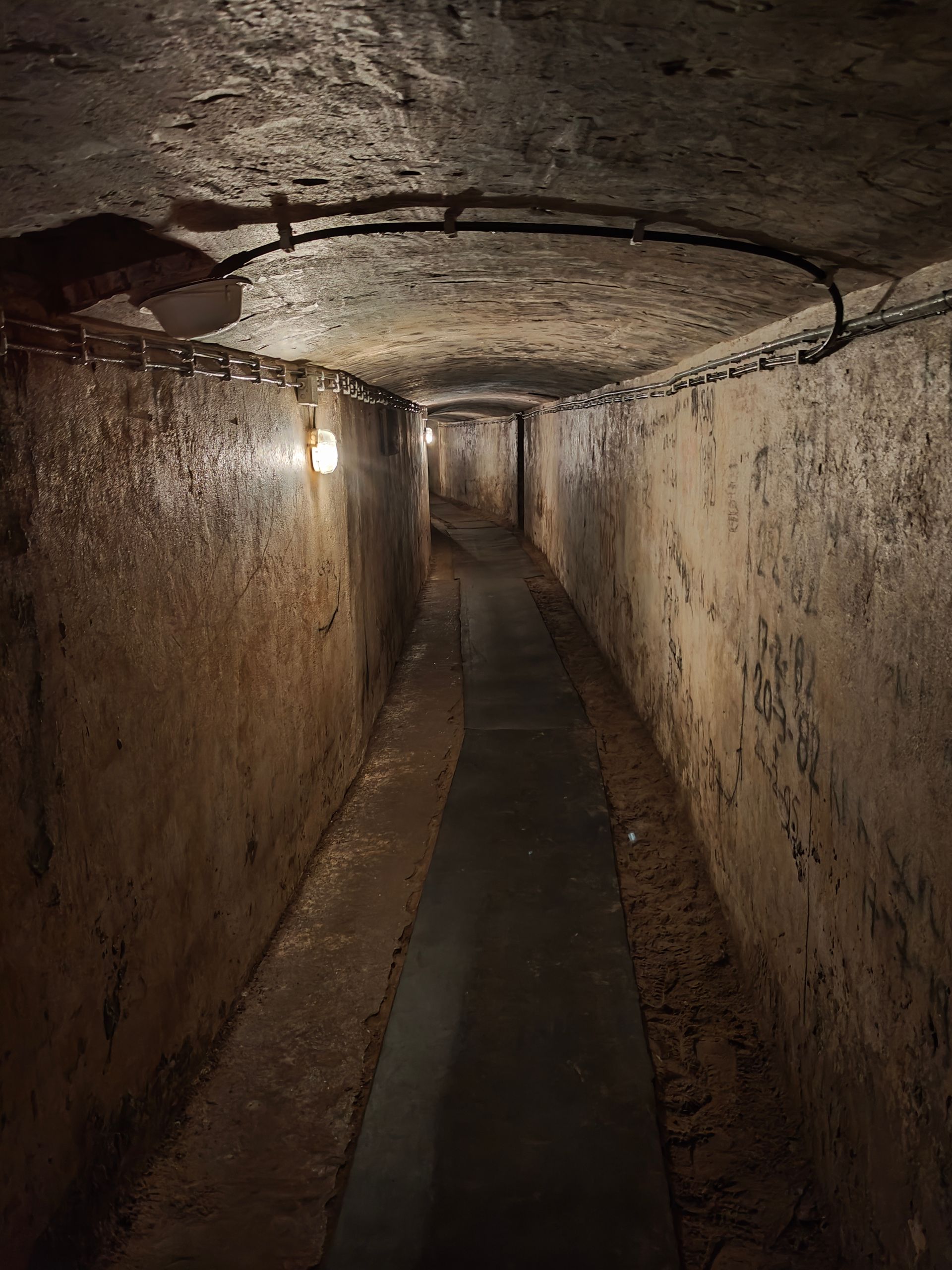 Smalle ondergrondse tunnel met ruwe betonnen muren en een zwak licht boven je hoofd.