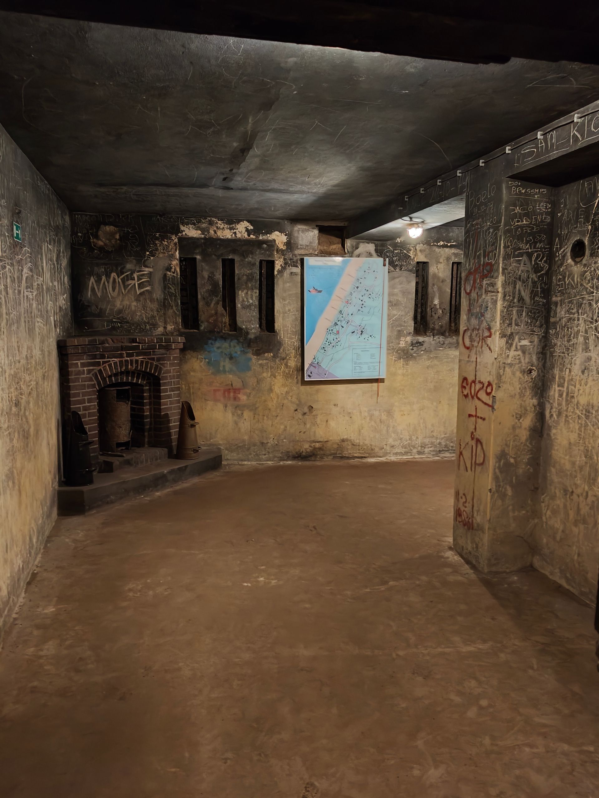 Een schemerige betonnen bunker met tralies voor de ramen, een laag plafond en een blauwe kaart aan de achterwand.