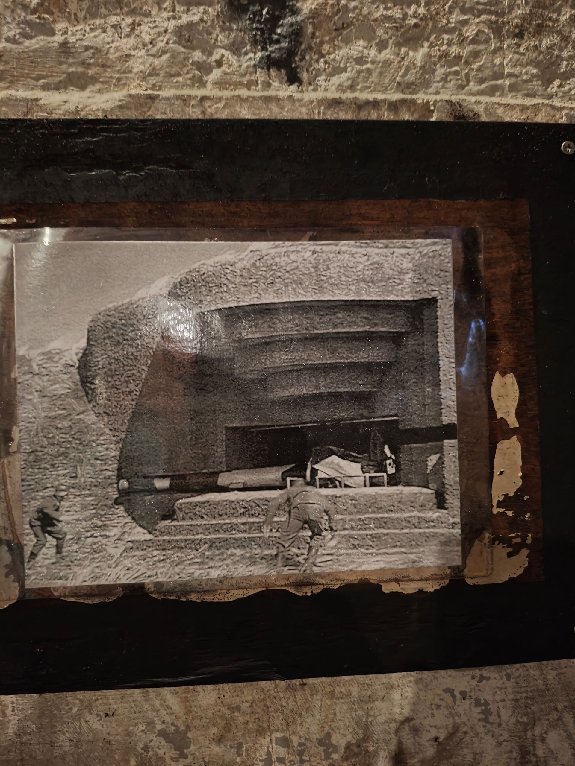 Beschadigde ingelijste zwart-witfoto aan de muur, met gescheurde randen en donkere omlijning.
