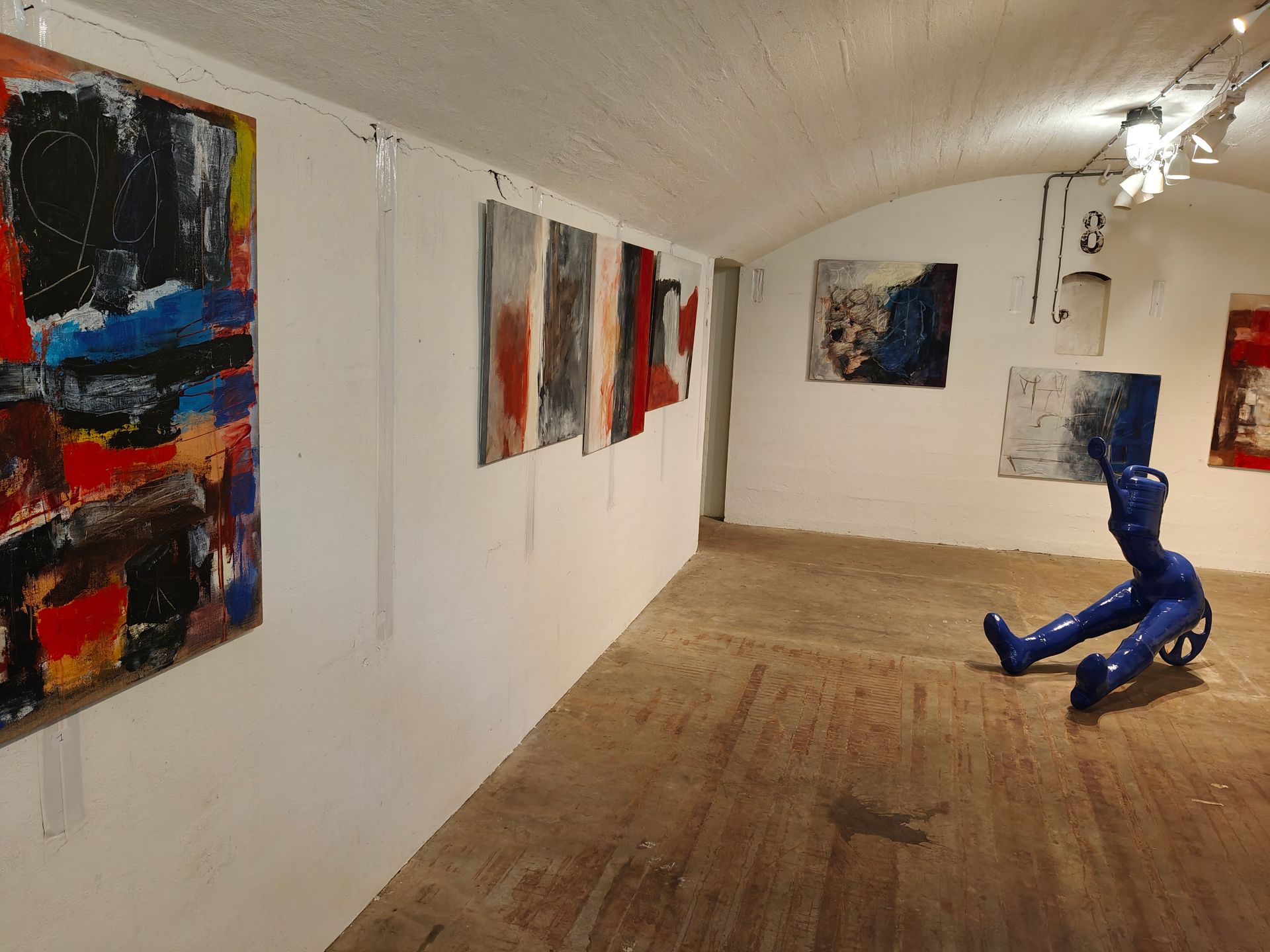 Kunstgalerie met abstracte schilderijen op witte muren en een blauwe sculptuur op de houten vloer.