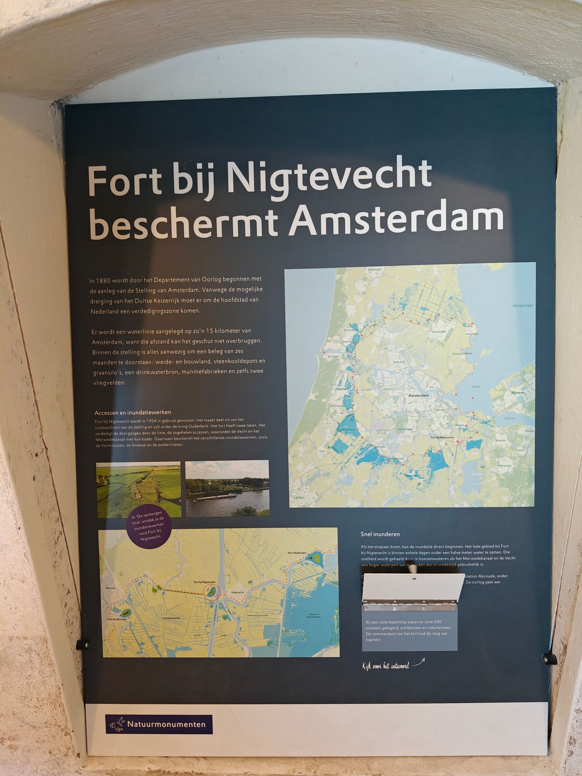 Museum sign about Fort bij Nigtevecht protecting Amsterdam, with maps and photos on a dark blue panel