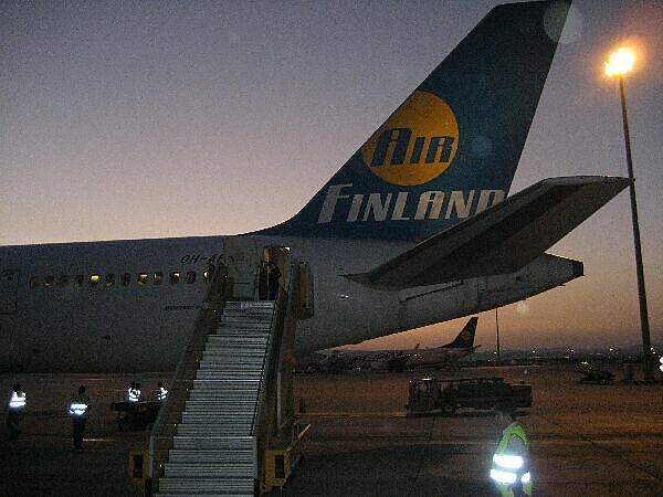 Een Finnair-vliegtuig bij schemering, met de instaptrap en het luchthavenpersoneel zichtbaar.