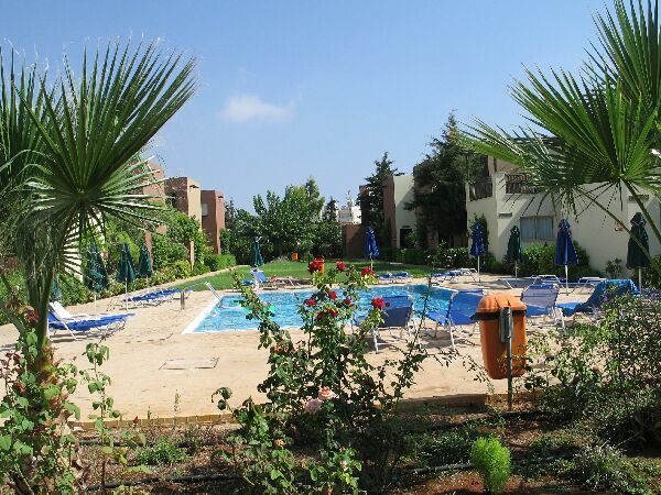 Zwembad van het resort met blauwe parasols, palmbomen en ligstoelen, omgeven door groen.
