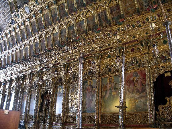 Rijkelijk versierd en verguld kerkinterieur met beschilderde iconen, gewelfde zuilen en hangende kandelaars en lampen.
