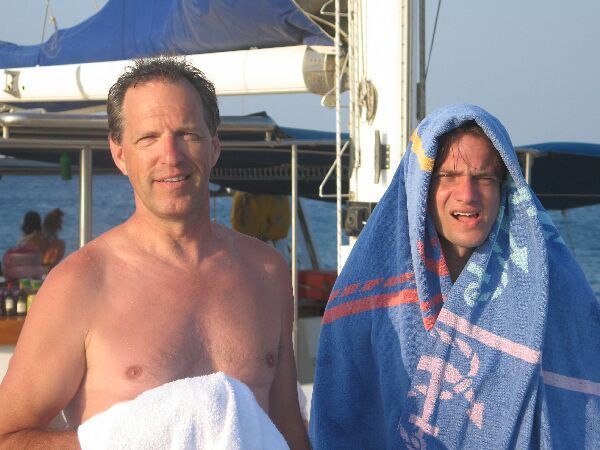 Twee mensen staan ​​buiten, gehuld in handdoeken, bij een boot; een van hen draagt ​​een blauwe handdoek over zijn hoofd.