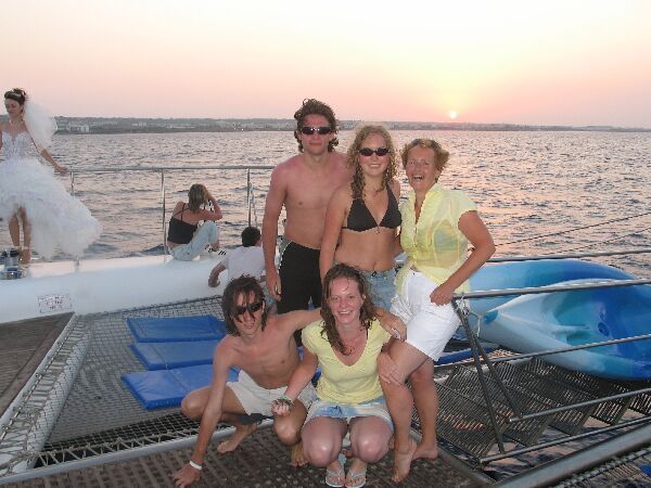 Mensen poseren op het dek van een boot bij zonsondergang met de oceaan op de achtergrond.