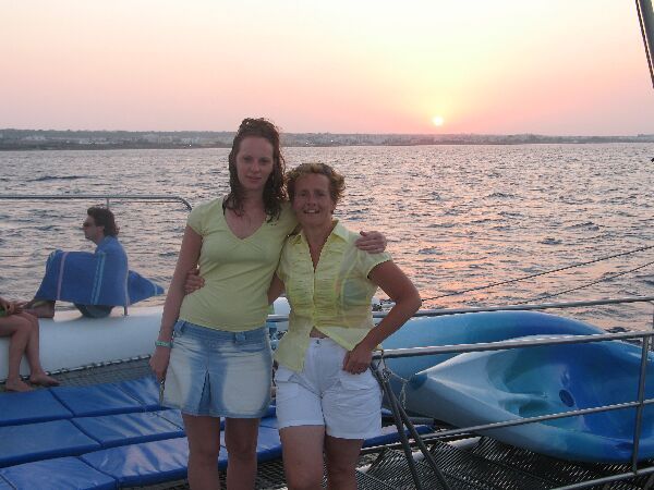 Twee vrouwen poseren op een boot bij zonsondergang op kalm water.