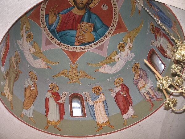 Muurschildering in de kerkkoepel met een heilige in het midden, engelen en in gewaden geklede figuren rond een klein raam.
