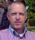 Een man in een rood-blauw gestreept shirt kijkt voor zich uit met een neutrale uitdrukking.