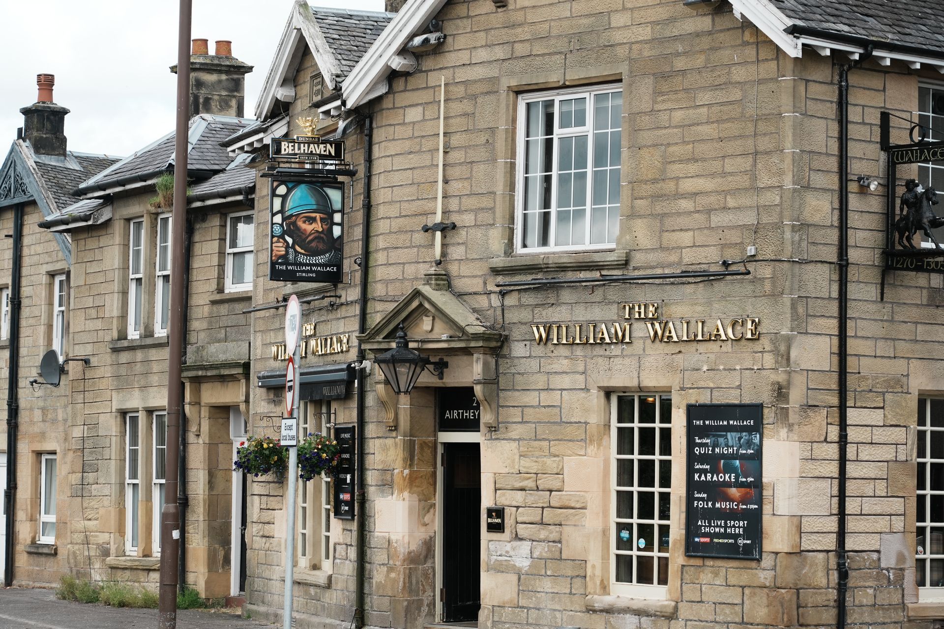 De buitenkant van de pub The Old Inn, een stenen gebouw met een uithangbord met een portret van een man, Schotland.