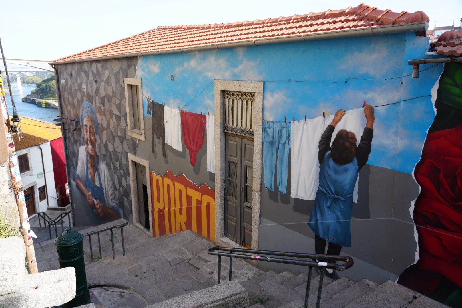 Muurschildering van een vrouw die de was ophangt in Porto, Portugal. Het gebouw heeft een geschilderde hemel.