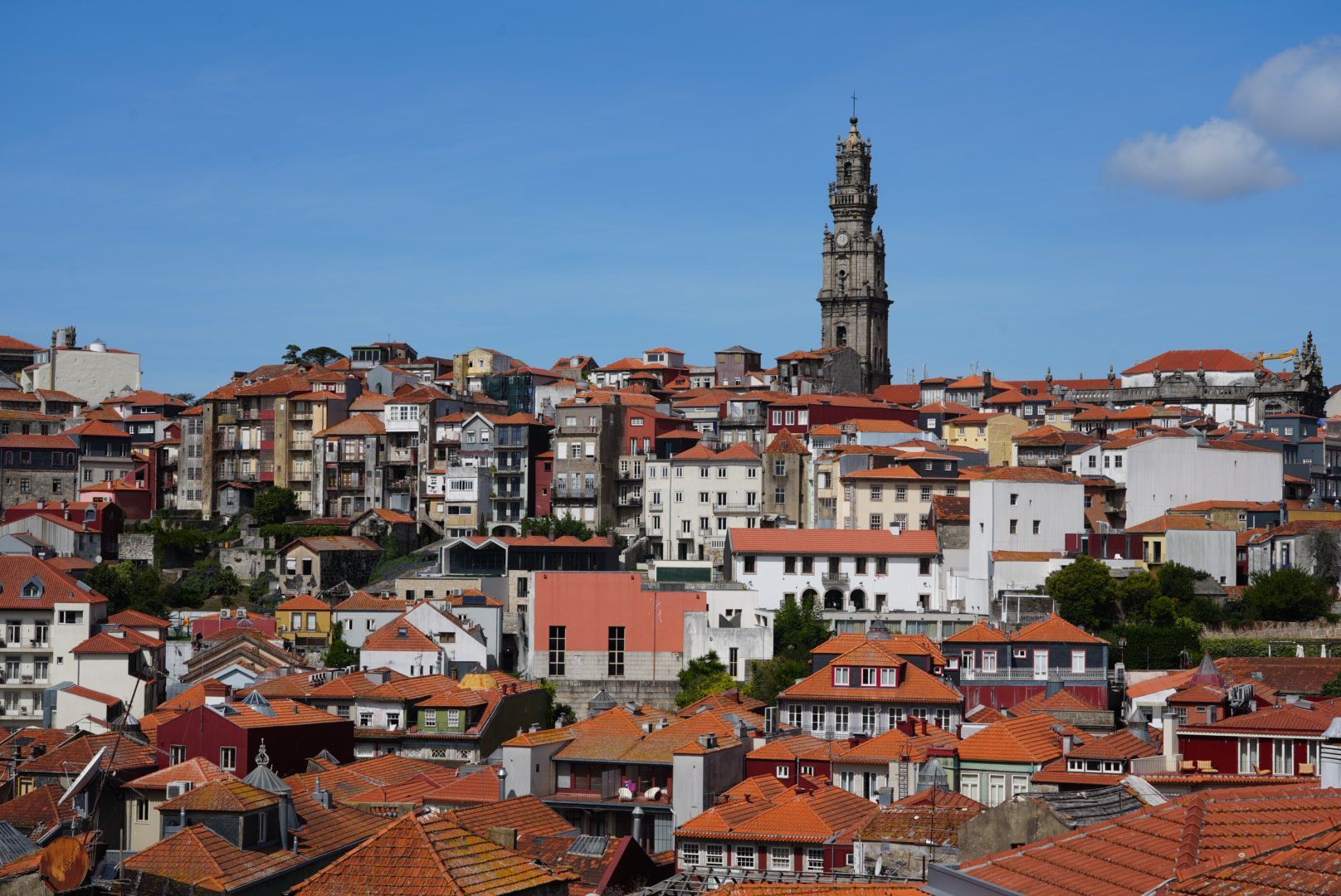 Stadsgezicht van Porto, Portugal, met oranje pannendaken, gebouwen en de toren van de Clérigoskerk tegen een blauwe lucht.