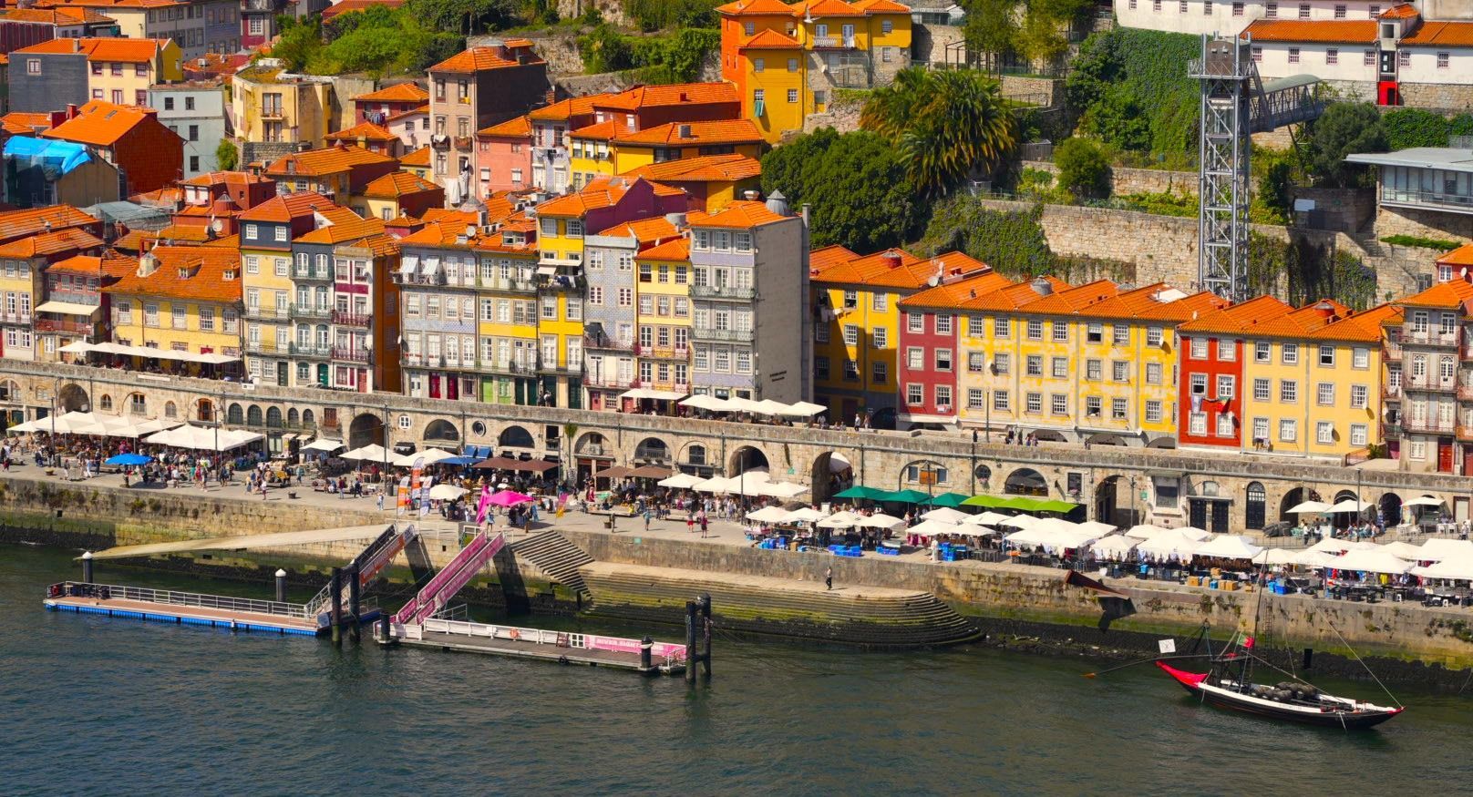 In Porto, Portugal, staan ​​kleurrijke gebouwen langs de rivieroever, met boten en mensen in het zicht.