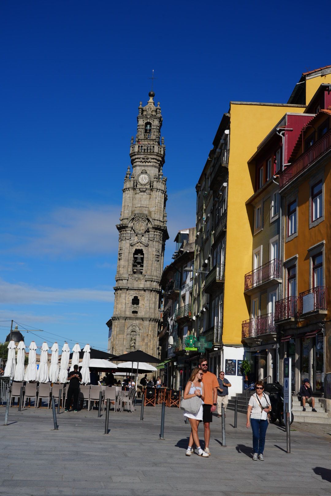 Een hoge stenen toren torent boven een plein met kleurrijke gebouwen uit in Porto, Portugal, onder een blauwe hemel.