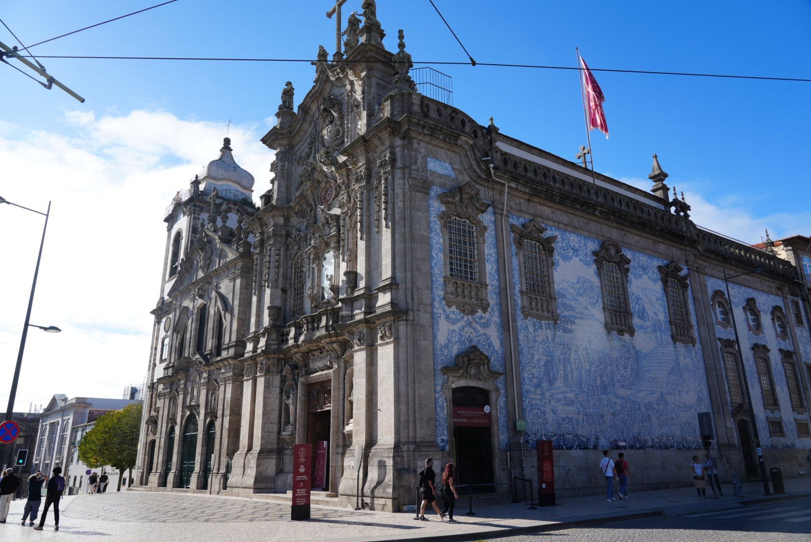De buitenkant van een kerk met een sierlijke gevel, een zijgevel van blauwe tegels, Porto op een zonnige dag.