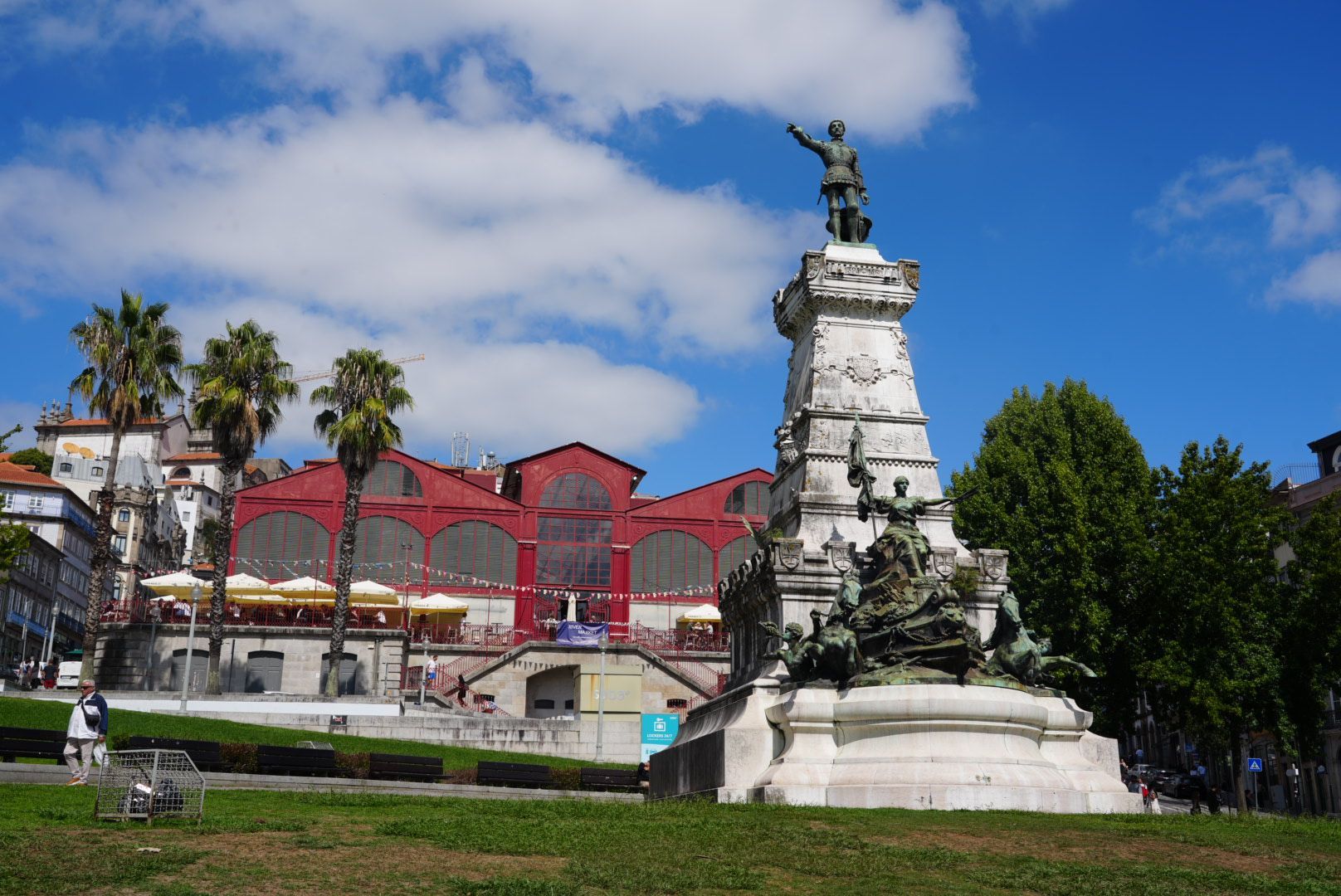 Standbeeld van een man bovenop een pilaar in Porto, Portugal. Op de achtergrond een marktgebouw.