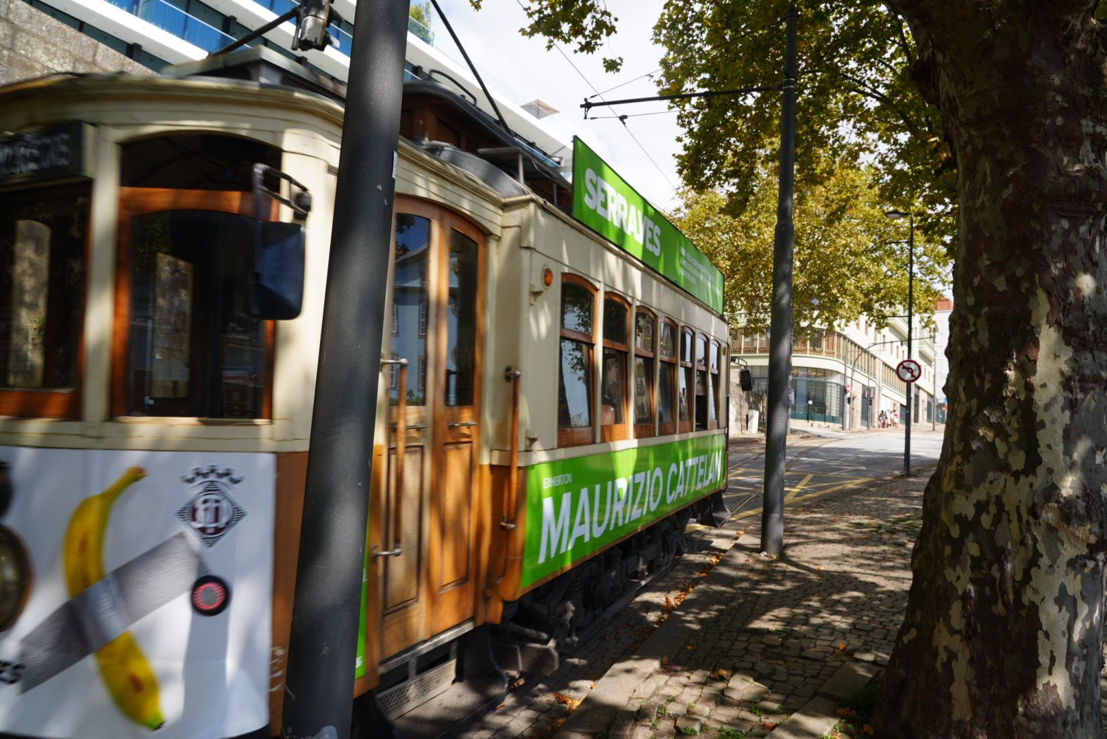 Een crèmekleurige en groene vintage tram op rails, geparkeerd in een straat met bomen.