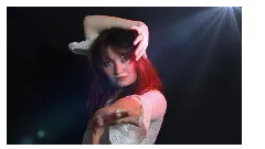 Vrouw in een witte kanten blouse, rood haar, handen bij het gezicht, poseert voor een donkere achtergrond met een lensflare.