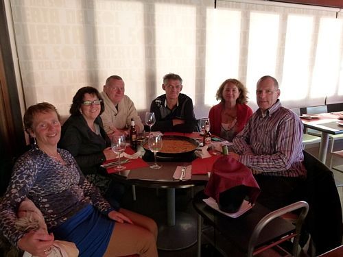 Zes mensen zitten rond een tafel in een restaurant en genieten van eten en drinken.