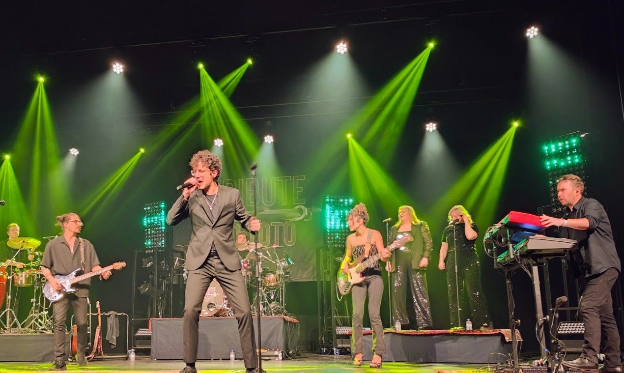 Band treedt op het podium op, zanger in beeld, groene podiumverlichting.