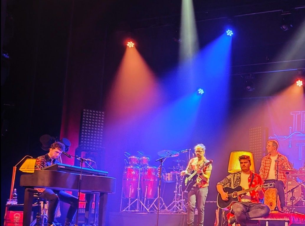 Band treedt op op het podium onder blauwe en rode spotlights.
