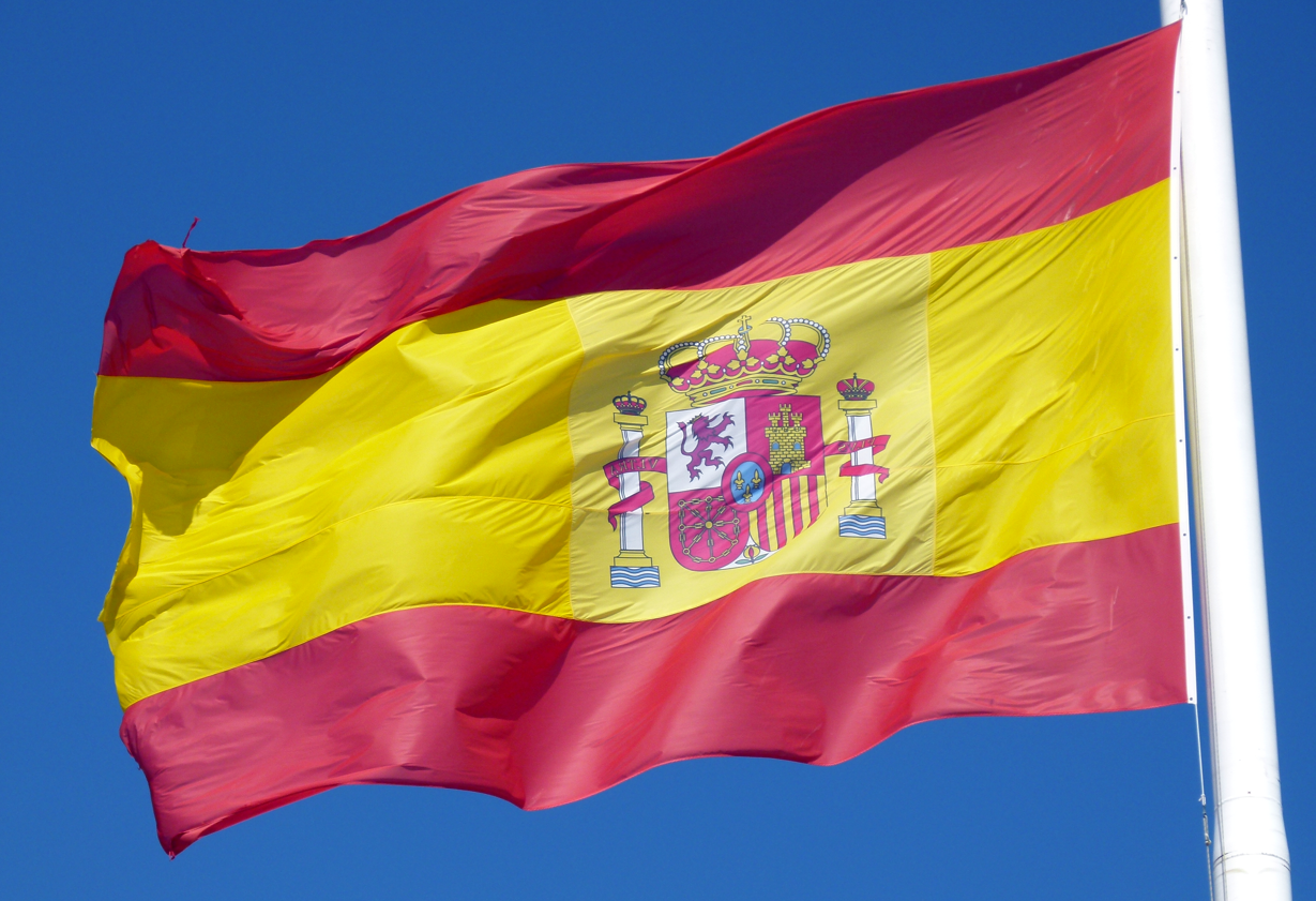 De Spaanse vlag wappert tegen een helderblauwe hemel. Rode en gouden horizontale strepen met een wapen.
