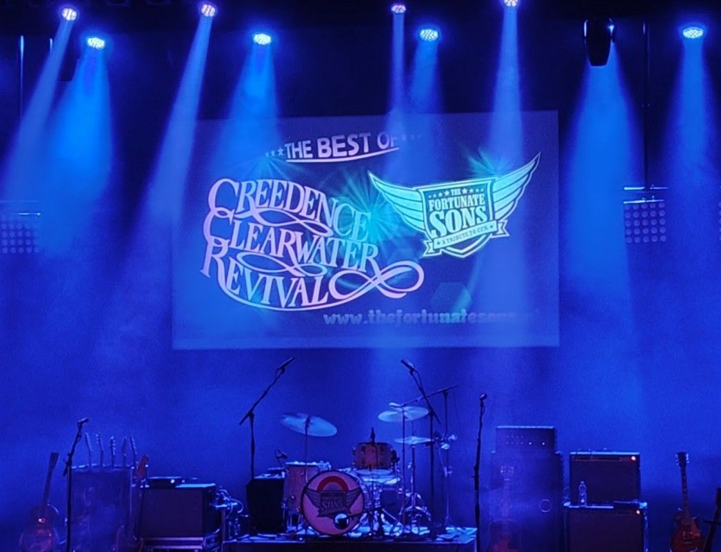 Het podium is klaargezet voor een Creedence Clearwater Revival-tributeconcert, compleet met blauwe podiumverlichting.