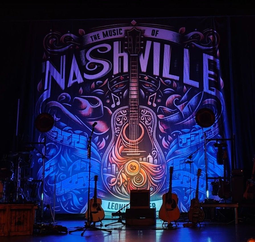 Podiumopstelling met een Nashville-muziekbanner, gitaren en instrumenten, verlicht door blauw licht.