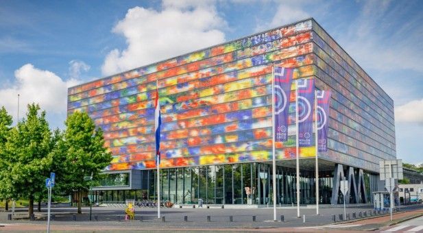Modern gebouw met een kleurrijke, gepixelde gevel en glazen wanden; vlaggen aan de voorkant.
