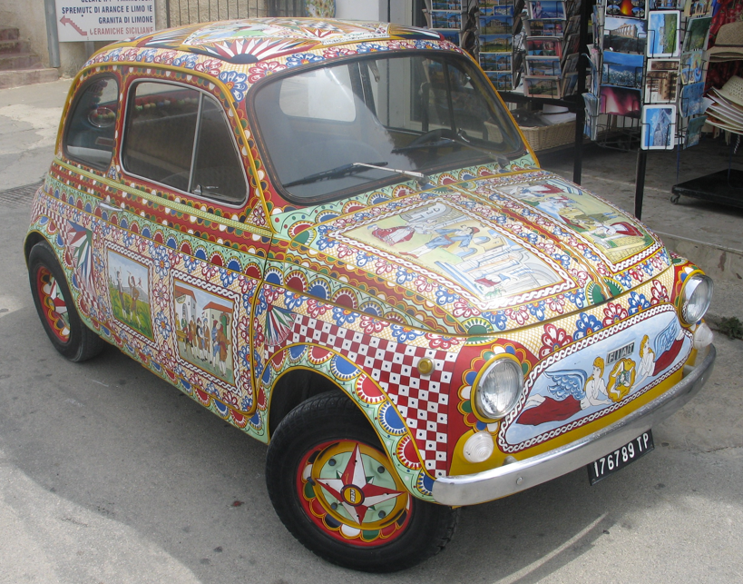 Een Fiat 500, versierd met kleurrijke volkskunstmotieven, staat geparkeerd op straat.