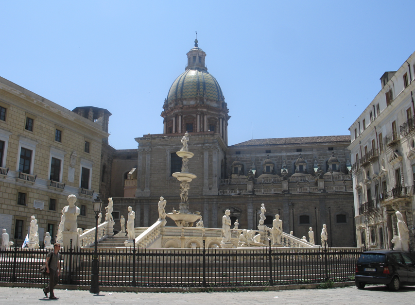 Fontein met beelden voor een gebouw met een koepel, Palermo, Italië. Omringd door een zwart hek.