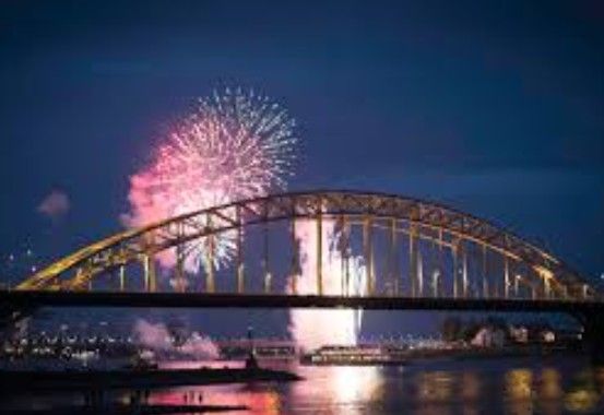 Vuurwerk dat 's nachts boven een gebogen brug explodeert; de weerspiegelingen ervan in het water.