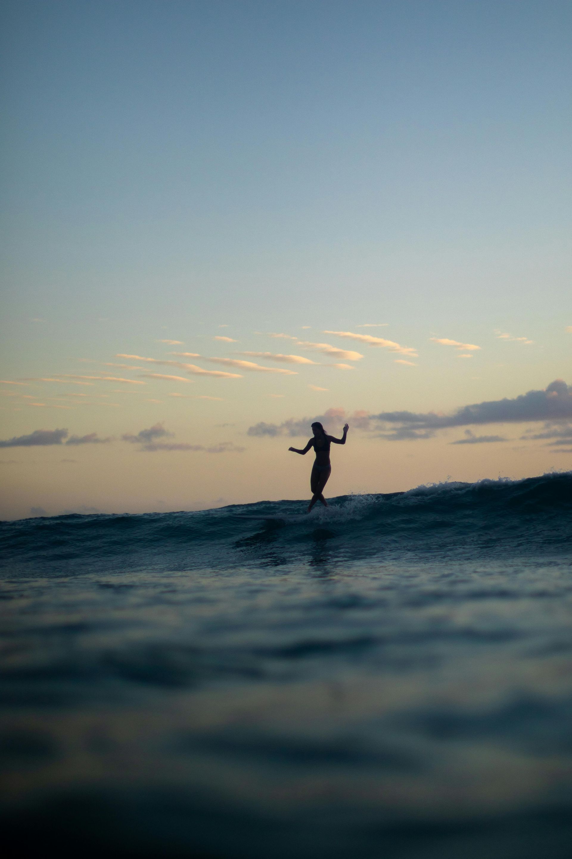 Een surfer die op een golf rijdt bij zonsondergang, zijn silhouet tegen de hemel.