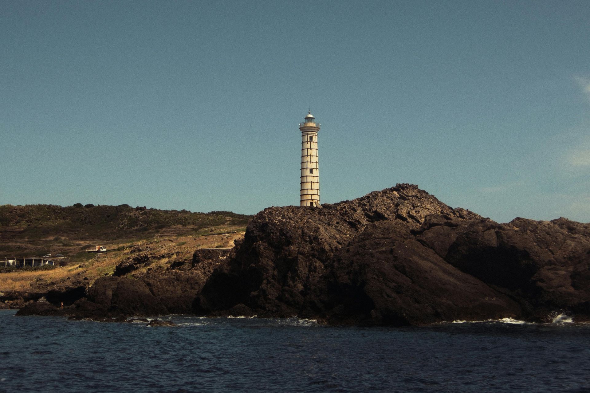 Vuurtoren op een rotsachtig eiland; blauwe lucht en water.