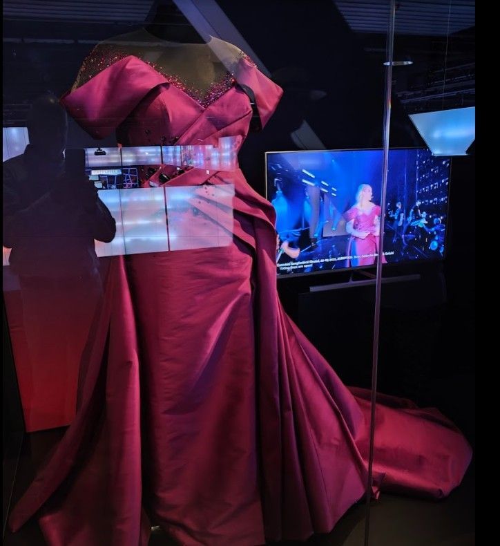 Een formele bordeauxrode avondjurk hangt aan een paspop in een vitrine. 