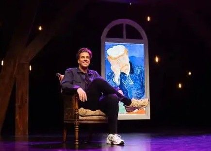 Een man zit in een fauteuil met een schilderij van Van Gogh achter hem op een podium.