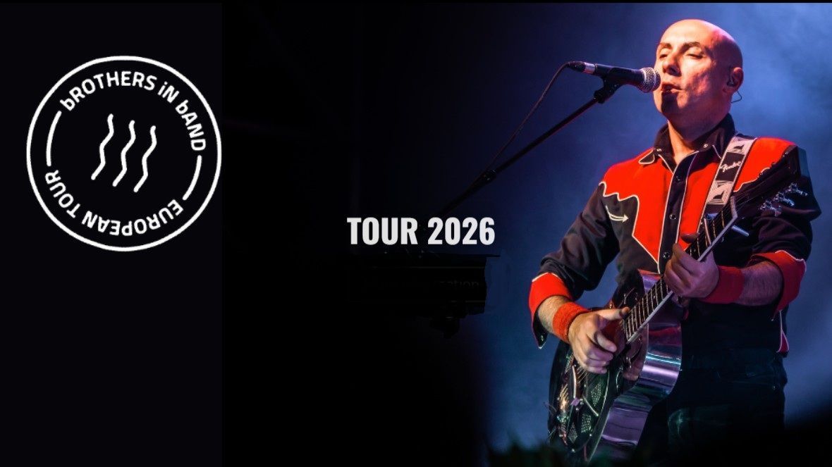 Een band treedt op een podium op met keyboards, drums en saxofoon in een concertsetting met spotlights.