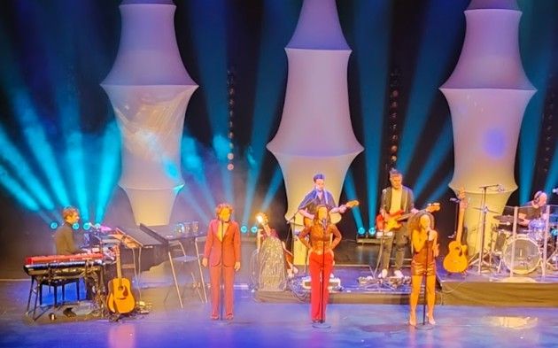 Band treedt op op een podium met kleurrijke lichten en een unieke achtergrond.