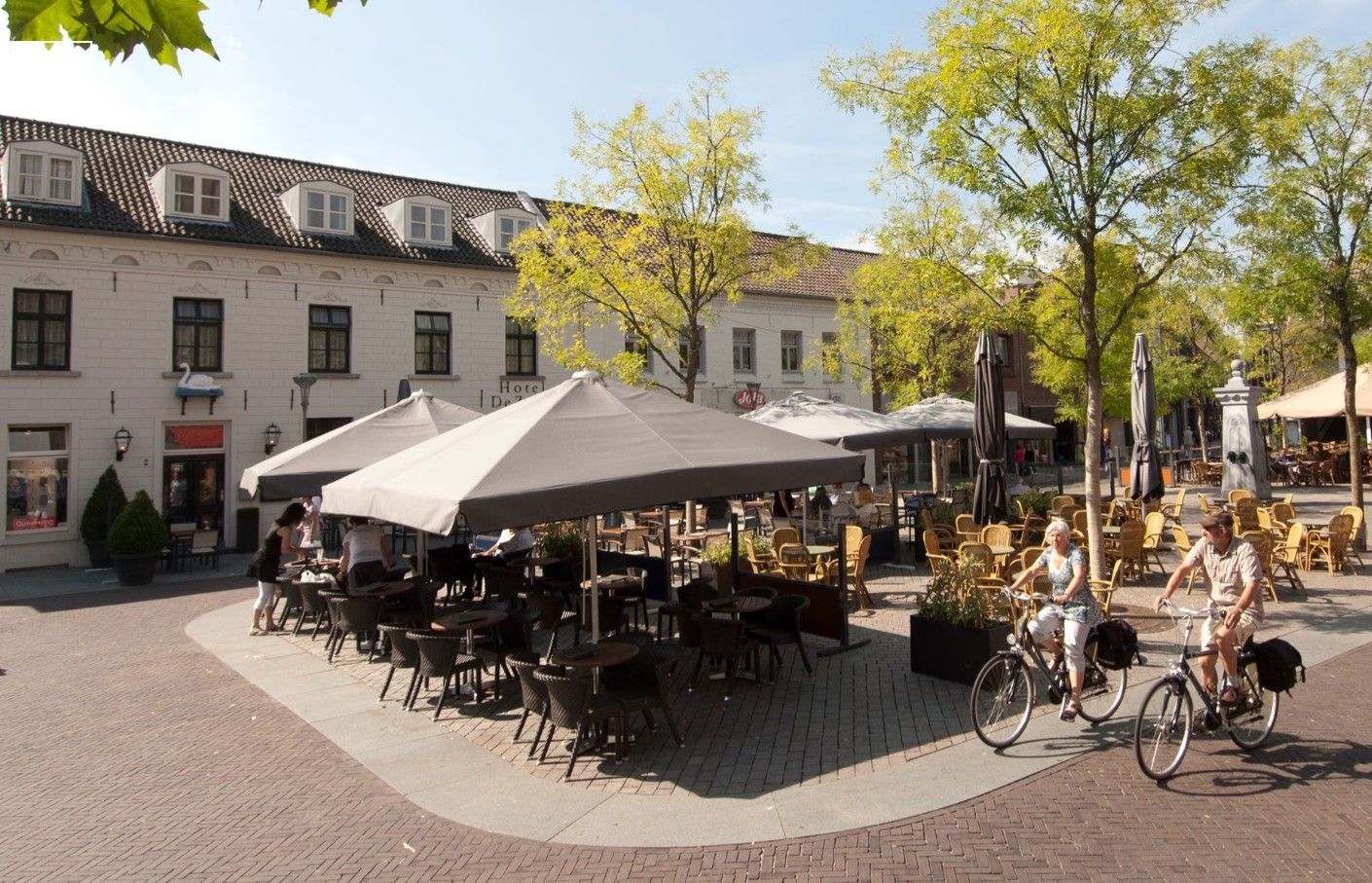Een terrasje met tafels, parasols en mensen. Doet denken aan centrum Venray