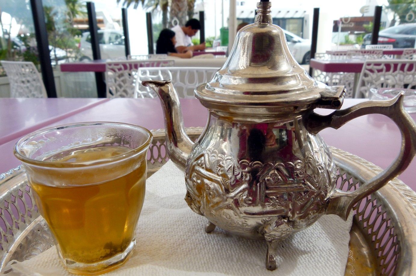 Marokkaans theeservies: sierlijke zilveren theepot, glas thee, op een dienblad. Paarse tafel, terras.