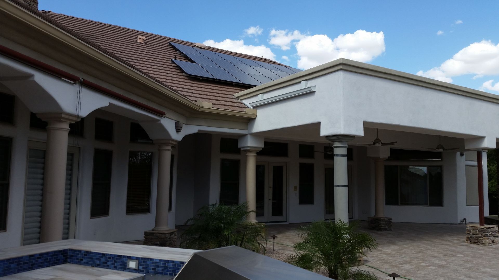 Single-story house with white columns, tiled roof, and a front courtyard under a blue sky.