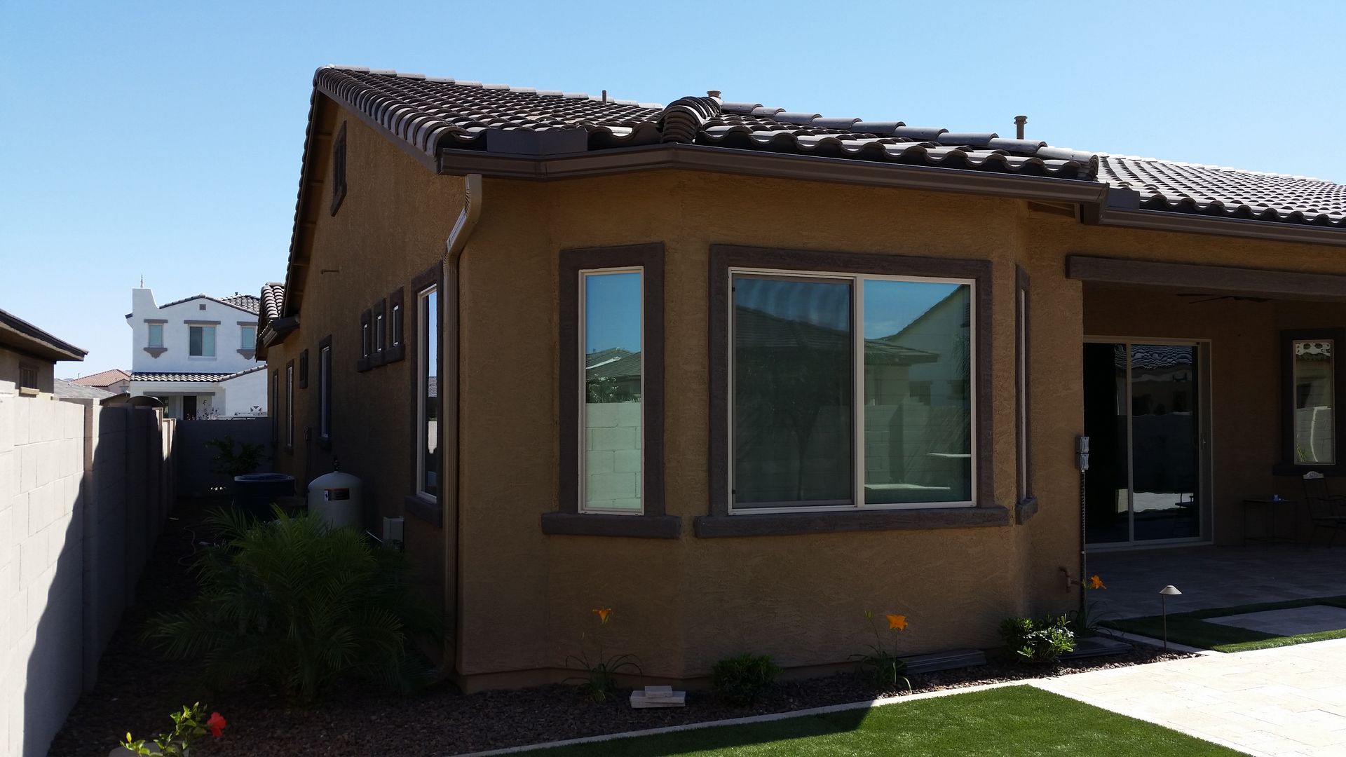 Exterior of a tan house with a tiled roof, large windows, and a small lawn beside a side yard.